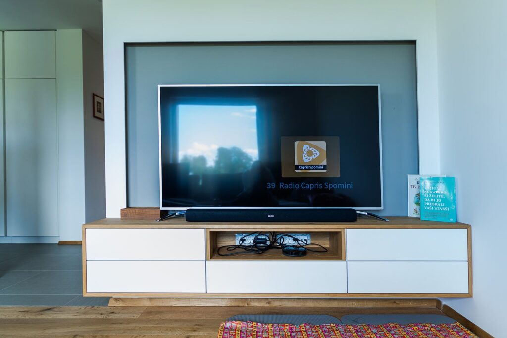 Dnevni prostor z belim TV elementom in hrastovo polico